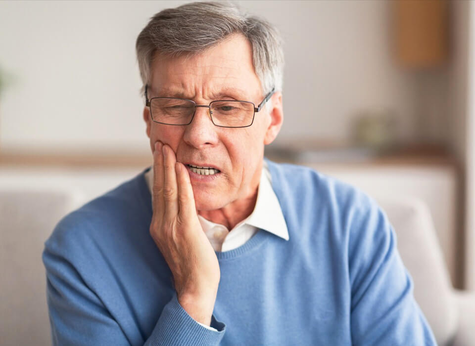 An older man with eye glasses holding his mouth right side and feeling tooth pain