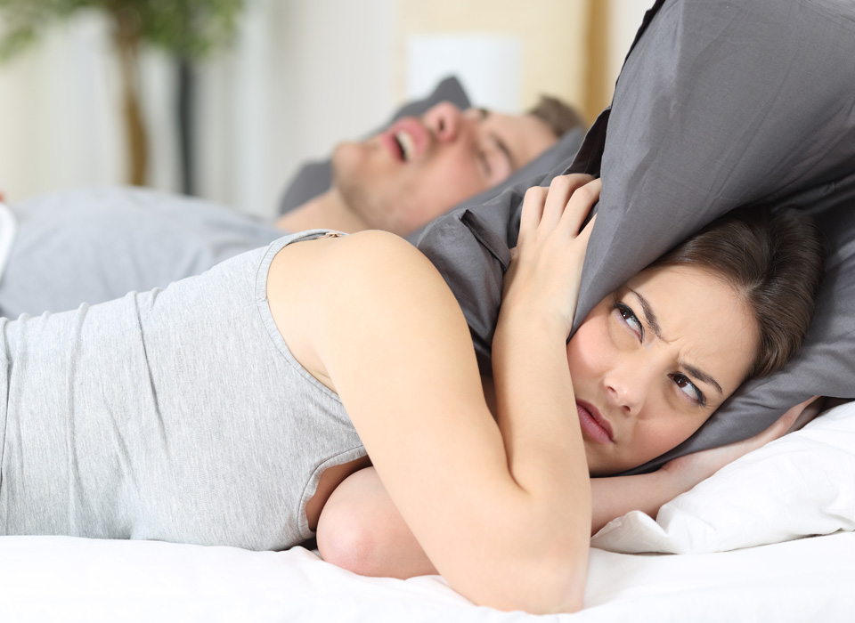 A girl covers her ears with pillows as she cant able to listen her partner's snoring on bed